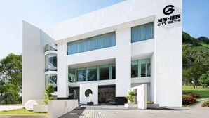 A modern building with a white facade, large windows, and a logo on the right side.