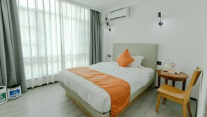 A hotel room with a bed, a chair, a small table with a tray, and an air conditioning unit on the wall.