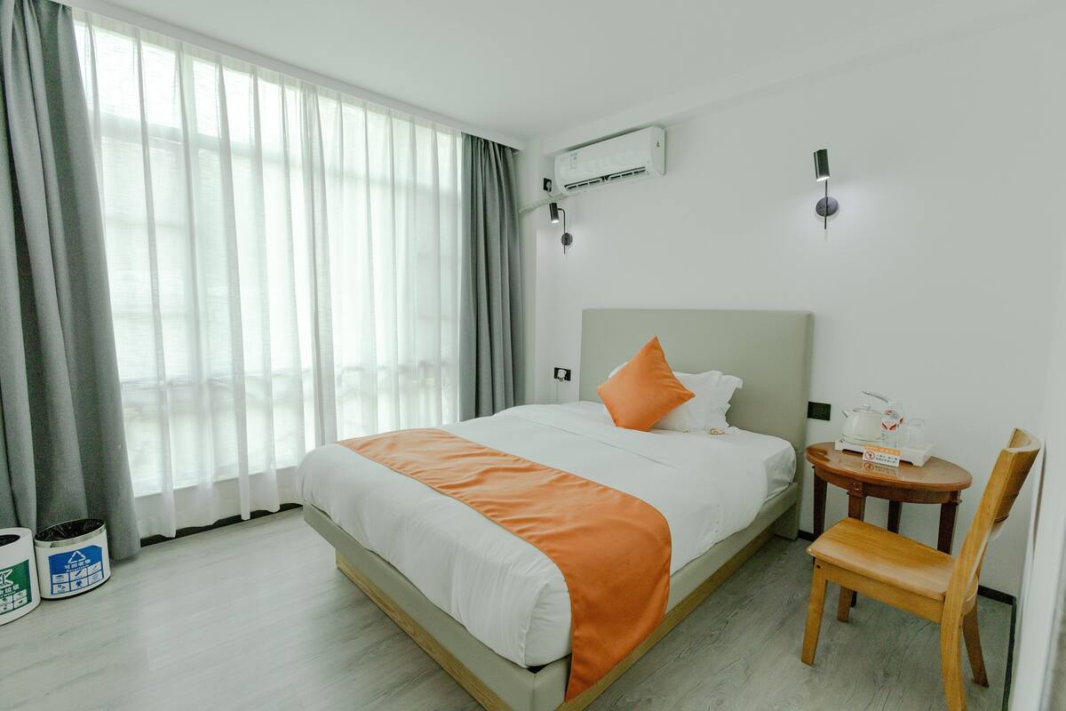 Hotellihuoneessa on sänky, tuoli, pieni pöytä, jossa on tarjotinalusta, sekä seinälle asennettu ilmastointilaite.
