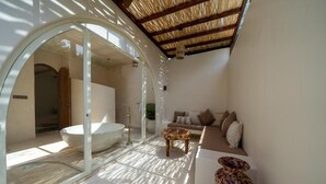 Un baño moderno con una bañera grande, un área de ducha con mampara de vidrio y una zona de estar con sofá y jarrón decorativo.