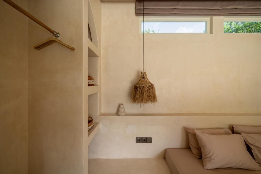Una habitación con una cama, una lámpara colgante, una ventana y un estante en la pared.