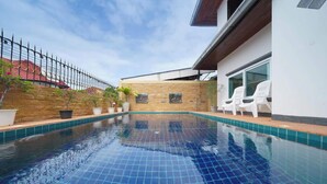 Una piscina con bordo piastrellato, un muro in pietra e un edificio bianco con una finestra e delle sedie.