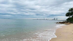 Una spiaggia con acque limpide, un litorale sabbioso e una skyline cittadina in lontananza, sotto un cielo nuvoloso.