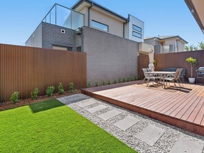 Un patio moderno al aire libre con terraza de madera, una mesa de comedor con sillas y una parrilla.