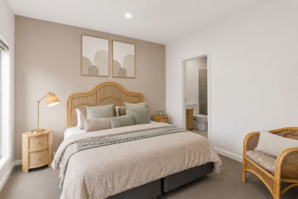 Een slaapkamer met een bed, nachtkastjes, een lamp, een stoel en een badkamer door een open deur zichtbaar.