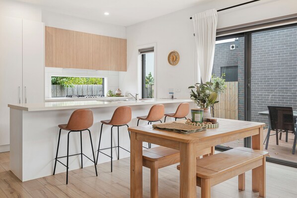 A modern kitchen with a central island, bar stools, and a dining table with benches. - Capel Haven House by Ready Set Stay (Capel Sound)