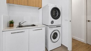 Cocina compacta con lavadora y secadora integradas, un lavamanos de acero inoxidable y una pequeña planta en maceta.