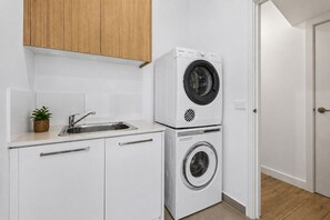 A compact kitchen with a built-in washer and dryer, a stainless steel sink, and a small potted plant. - Capel Haven House by Ready Set Stay (Capel Sound)