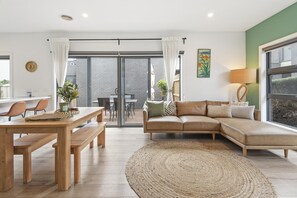 En moderne stue med et træbord, bænke, en sofa og en stor vævet måtte.