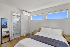 Ein modernes Schlafzimmer mit einem großen Bett, einem begehbaren Kleiderschrank und einem Badezimmer mit Glasdusche.