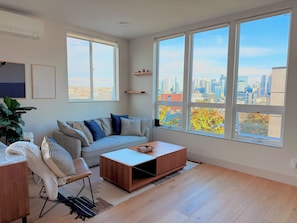 Ein modernes Wohnzimmer mit einer Couch, einem Couchtisch und großen Fenstern mit Blick auf die Stadt.
