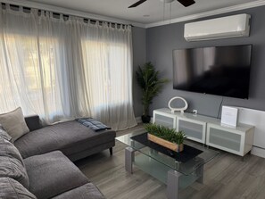 A modern living room with a grey sofa, a glass coffee table, a TV, and a ceiling fan. - Bring the family with lots of room only steps from the water in Mission Beach. (San Diego)