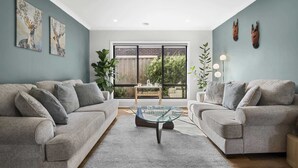 A living room with two grey sofas, a glass coffee table, and a large window with a view of greenery. - Garden Retreat 4-Bed House in Tarneit (Tarneit)