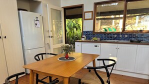 Una cocina con una mesa de madera, sillas, un refrigerador y una ventana con vistas al verdor.