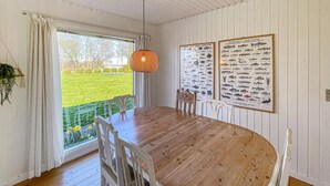 Een eetkamer met een houten tafel en stoelen, een hanglamp, en twee ingelijste viskaarten aan de muur.