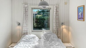 Een slaapkamer met een bed, raam, gordijnen en een schilderij aan de wand.