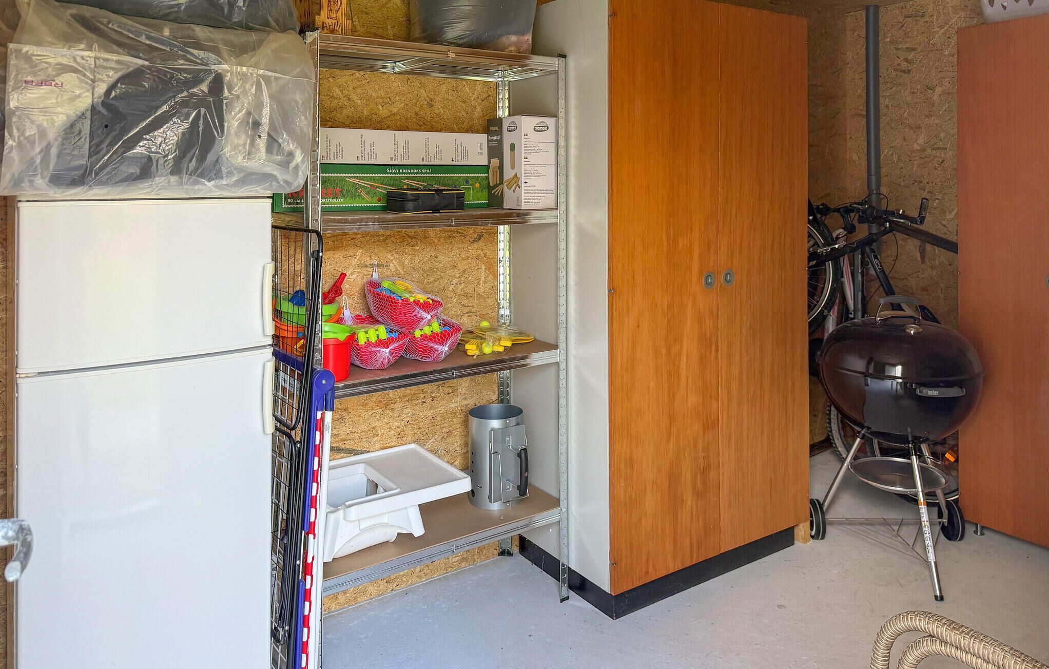 A compact kitchen with a refrigerator, a wooden cabinet, a grill, and various kitchen utensils.