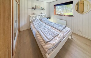 A single bed with a headboard, a bedside table, a small shelf with pictures, and a window with a view of trees. - Nice home in Rødby with WiFi (Rødby)