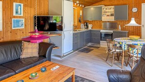 Een gezellig houten huisje van binnen, met een woonkamer, eethoek, keuken en een groot raam.