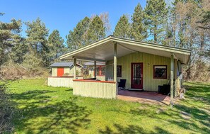 A small wooden cabin with a porch, a red door, and a small shed in a wooded area. - Nice home in Rødby with WiFi (Rødby)
