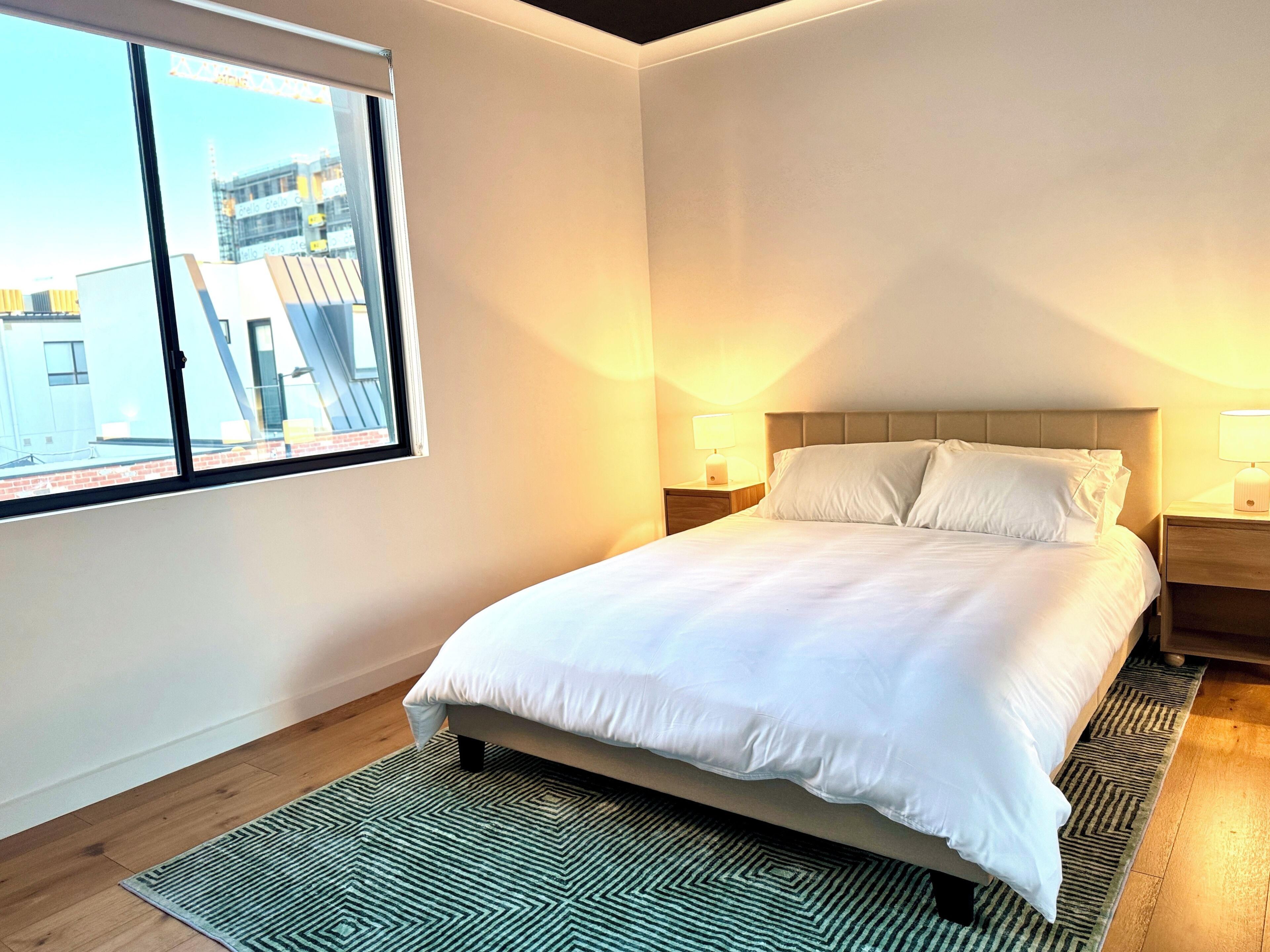Una camera da letto con un letto, due comodini, una finestra e vista sugli edifici.