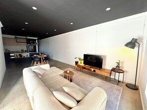Un soggiorno moderno con un divano componibile, una TV a schermo piatto, un tavolino e, sullo sfondo, un'area pranzo.