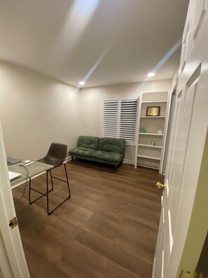 Ein Zimmer mit Schreibtisch, Stuhl, grünem Sofa und einem weißen Regal.