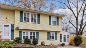 A two-story yellow house with green shutters, a front yard with grass and a few potted plants, and a visible mailbox. - 1-bedroom townhome in Odenton with guest share bath. (Odenton)