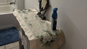 Une salle de bain avec une baignoire, un miroir, un lavabo doté d’un cache décoratif et des articles de toilette rangés sur une étagère.