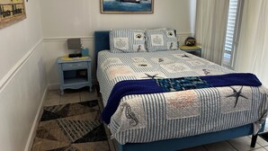 Une chambre à coucher comprenant un lit, une table de chevet, un climatiseur fixé au mur, un tableau et une fenêtre avec des rideaux.