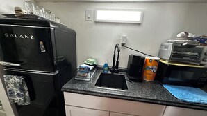 Une cuisine compacte comprenant un réfrigérateur noir, un évier, une machine à café, un four à micro-ondes et un grille-pain.