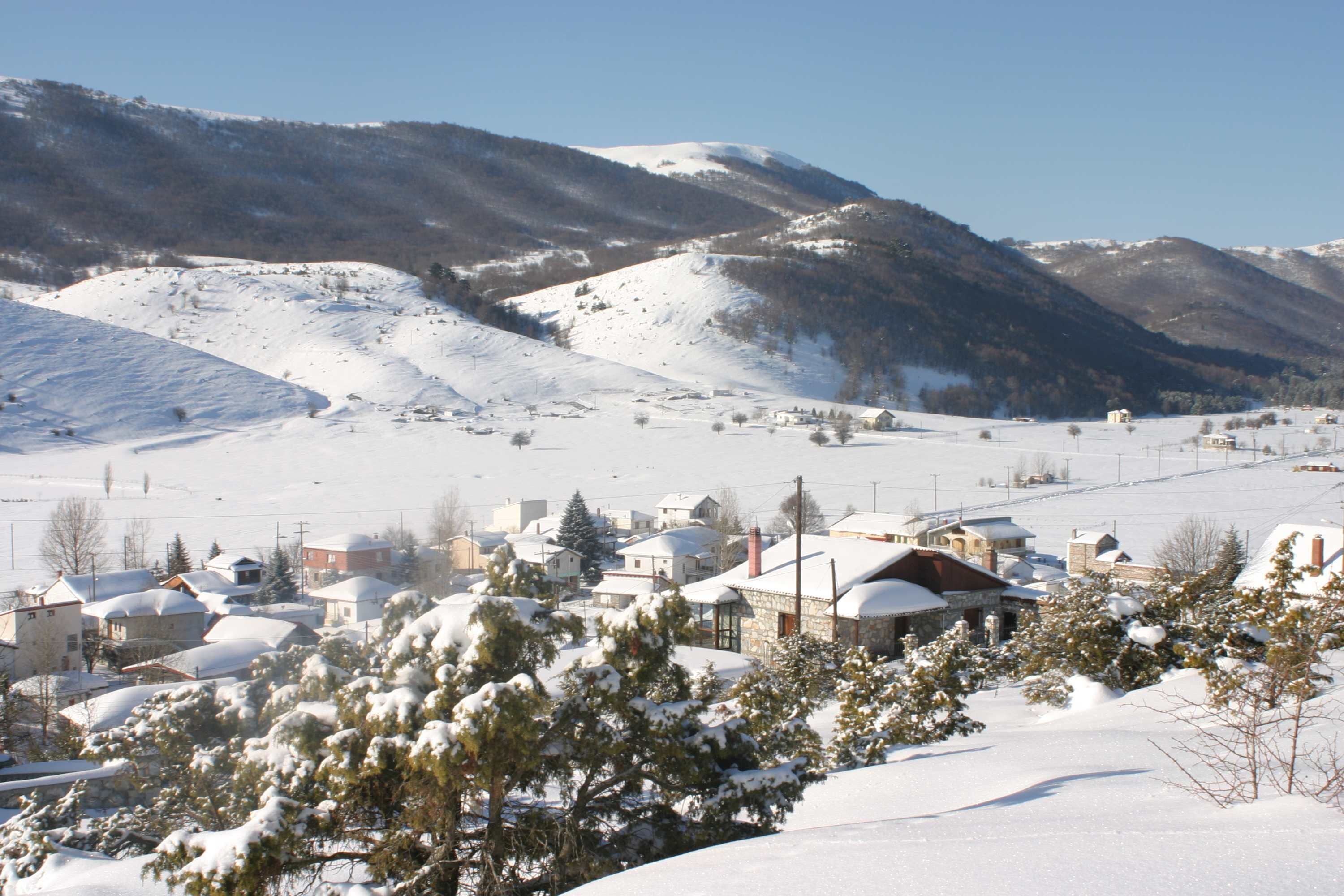 Un pueblo cubierto de nieve con casas, una iglesia y montañas al fondo.