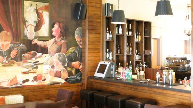 Zona de bar con paneles de madera, taburetes, una barra con diversas botellas y un cuadro grande de un caballo.