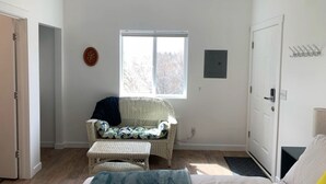 Ein Zimmer mit Korbsessel, kleinem Tisch, Fenster und Tür.