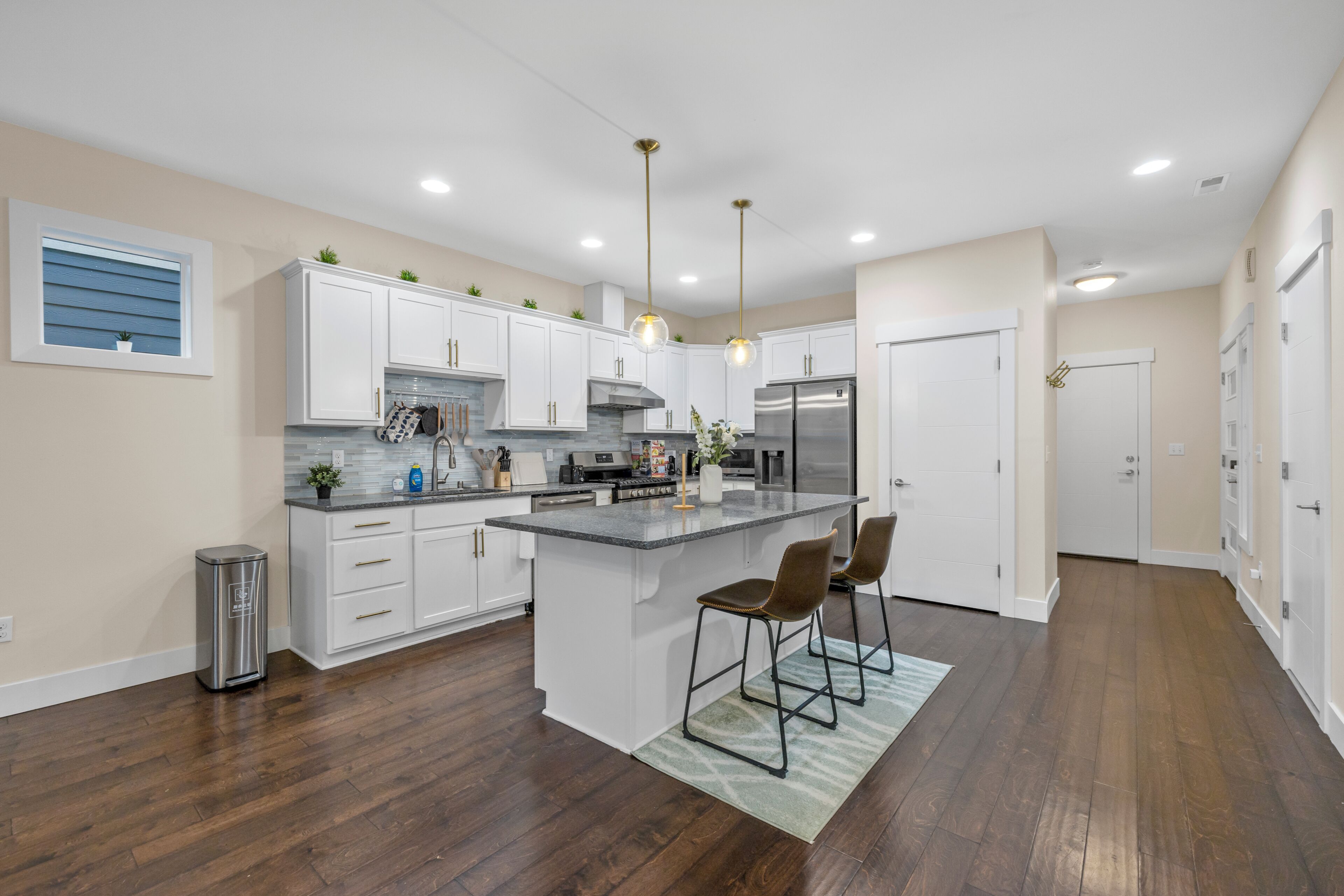 A modern kitchen with white cabinets, a central island, bar stools, and a stainless steel refrigerator.