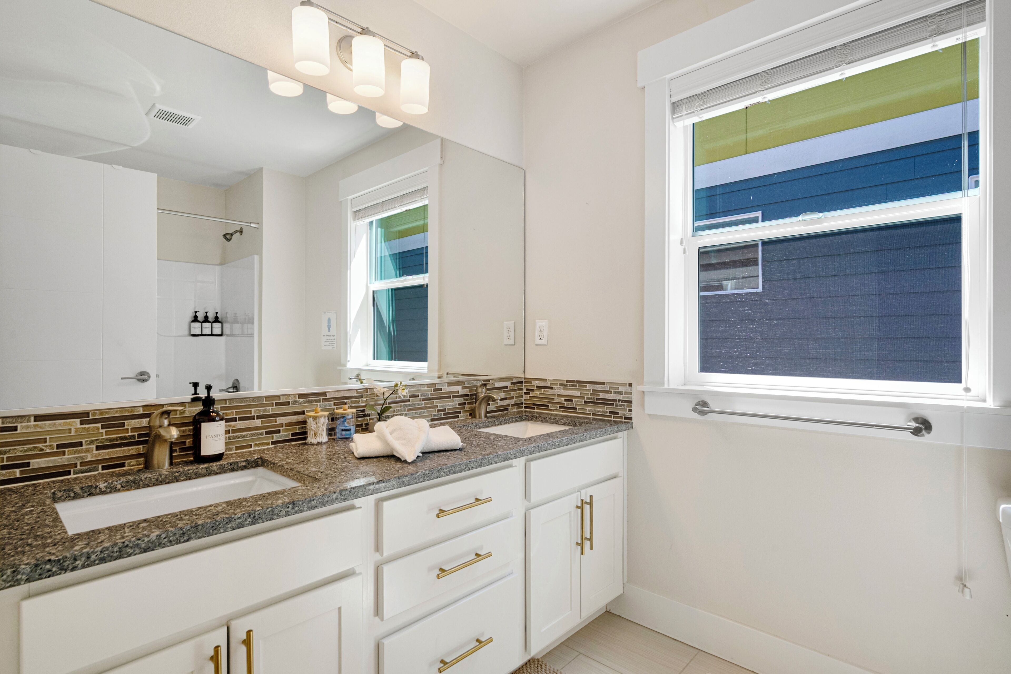 A bathroom with a double sink, a large mirror, and a window.