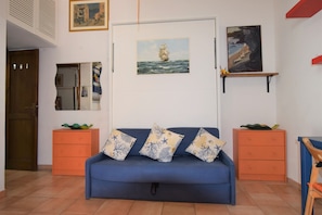 A living room with a blue sofa, orange side tables, a door, and wall-mounted artwork. - Beautiful equipped veranda (Fetovaia)
