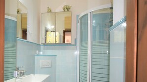 Ein Badezimmer mit Waschbecken, Toilette, Duschkabine mit Glastüren und Spiegel über dem Waschbecken.
