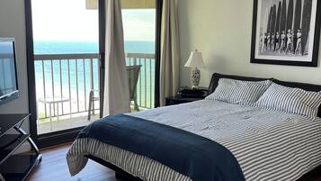 A hotel room with a bed, a TV, a balcony with a view of the sea, and a framed picture on the wall.