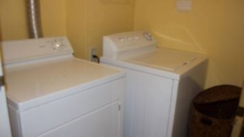 A laundry area with two white washing machines and a trash bin.