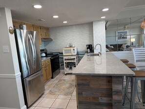 A modern kitchen with stainless steel appliances, a wooden island, and a tiled backsplash. - Oceanfront Spacious, 4 Bedroom Condo, Best Amenities & Views, Sleeps 12-14 (Ocean City)