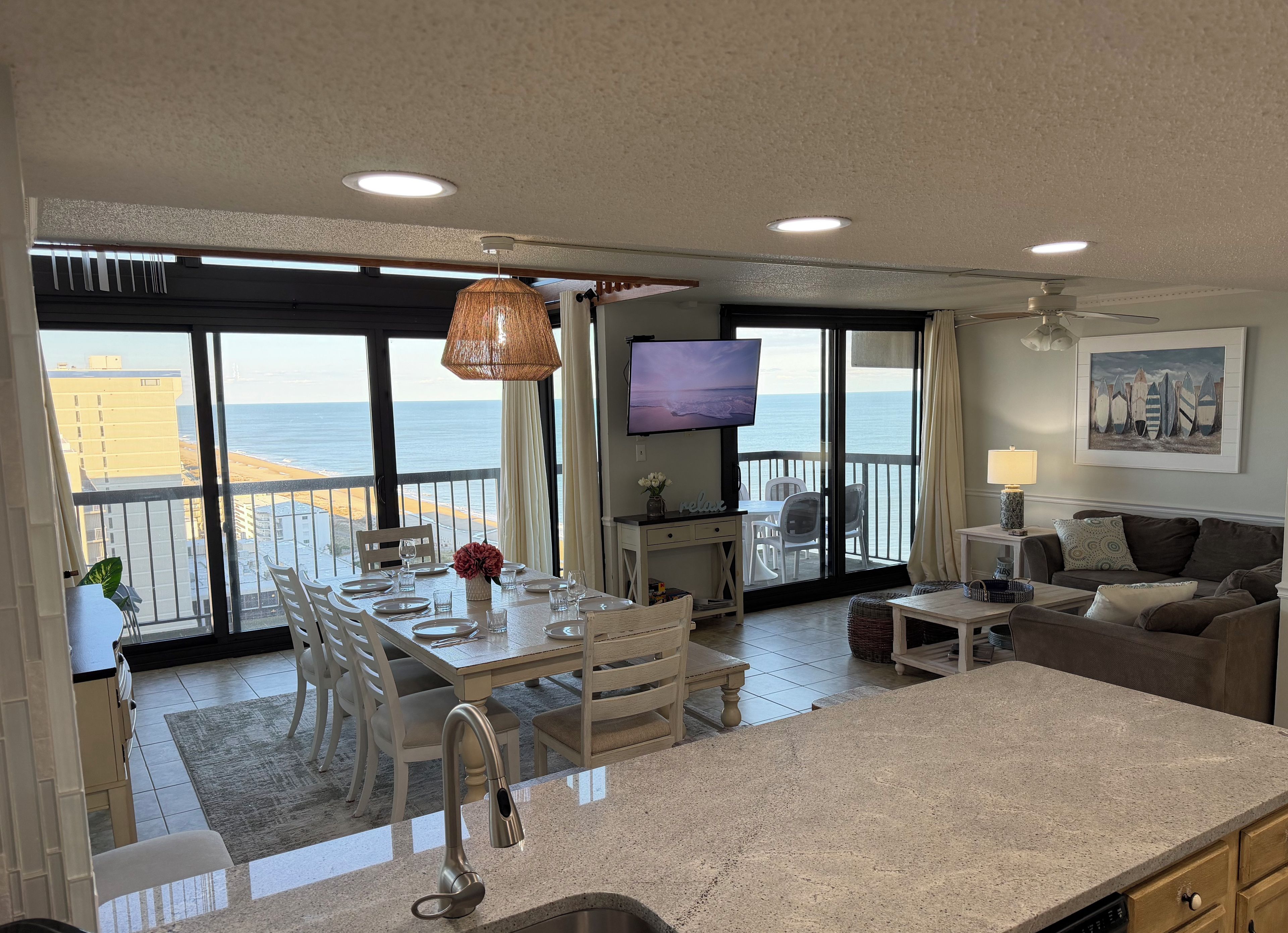 Zona saló àmplia amb un balcó que domina la platja, taula de dinar per a quatre i televisió de pantalla plana penjada a la paret.