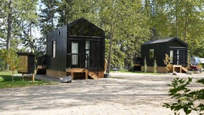 Two black cabins with wooden decks and windows, surrounded by trees.