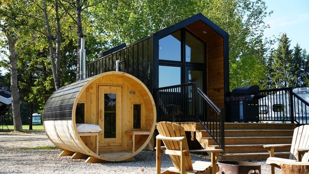 A cabin with a wooden exterior, a large window, and a deck with chairs.