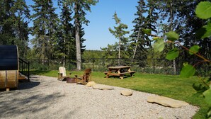 A gravel area with picnic tables and chairs, surrounded by a fence and trees.