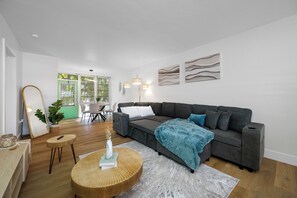 Ein modernes Wohnzimmer mit einem grauen Sofa, einem runden Couchtisch aus Holz und einem großen Spiegel.