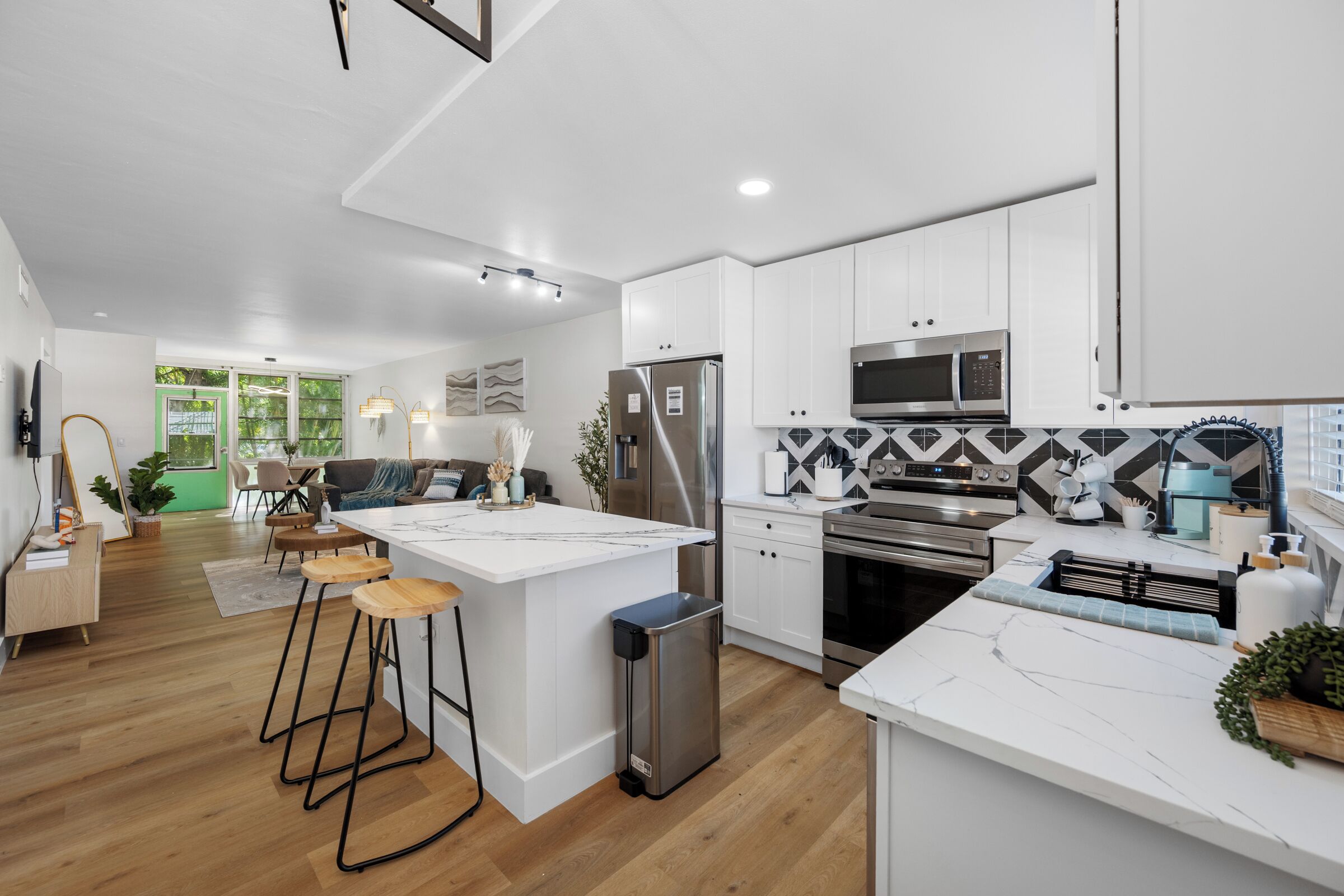 A modern kitchen with white cabinetry, a central island, bar stools, a stainless steel refrigerator, a microwave, and an oven.