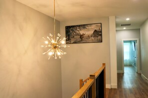 A hallway with a wooden railing, a hanging light fixture, and a framed picture on the wall. - Your cozy Texas home in Fort Worth! 5 min to Downtown FW (Fort Worth)
