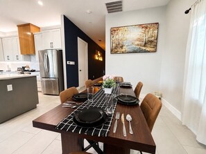 A modern kitchen with a dining area, featuring a stainless steel refrigerator, a dining table set for four, and a painting on the wall. - Broadway Homestead  Mins to Stockyards & Downtown (Fort Worth)