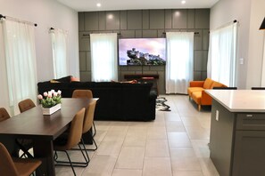 A modern living room with a sofa, dining table, and a flat-screen TV mounted on the wall. - Your cozy Texas home in Fort Worth! 5 min to Downtown FW (Fort Worth)
